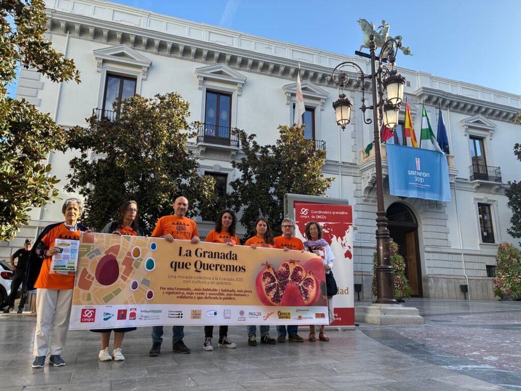 Representantes de las entidades de La Granada que Queremos, con camisetas naranjas de Pobreza Cero, sostienen la pancarta de la campaña frente al Ayuntamiento de Granada
